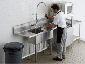 A large two-compartment commercial kitchen sink used for rinsing dishes, with a powerful pre-rinse spray