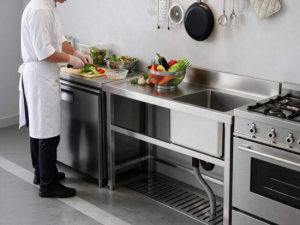 Commercial kitchen sink with table and integrated drainboard, used for food prep by a chef
